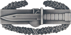 Metallic dagger badge with laurel wreaths on a white background